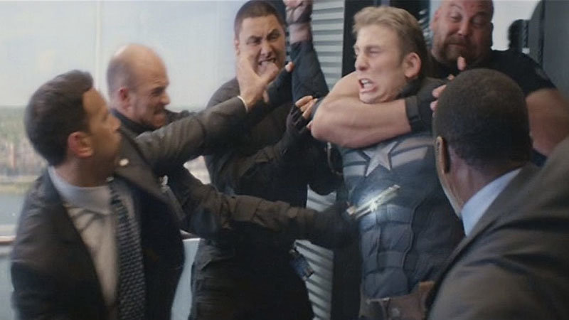 Captain America encerclé dans un ascenseur par des hommes en costume qui le maîtrisent, dans une bagarre confuse et tendue
