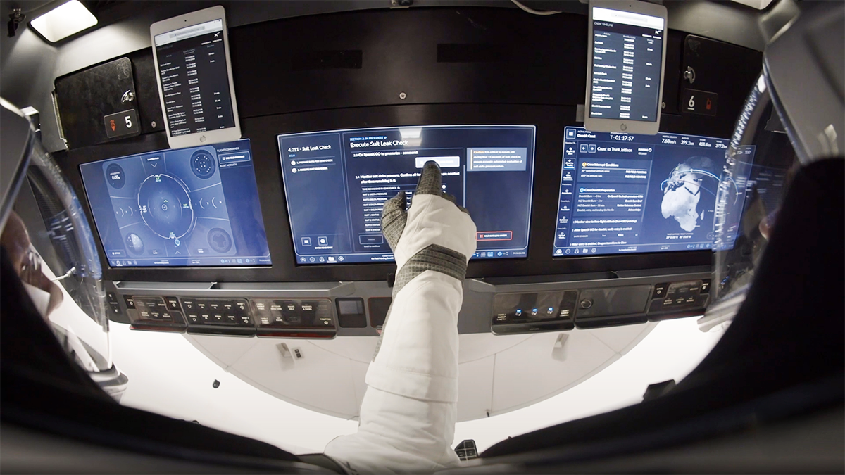 Écrans tactiles de la capsule Crew Dragon avec un astronaute en combinaison touchant l'interface