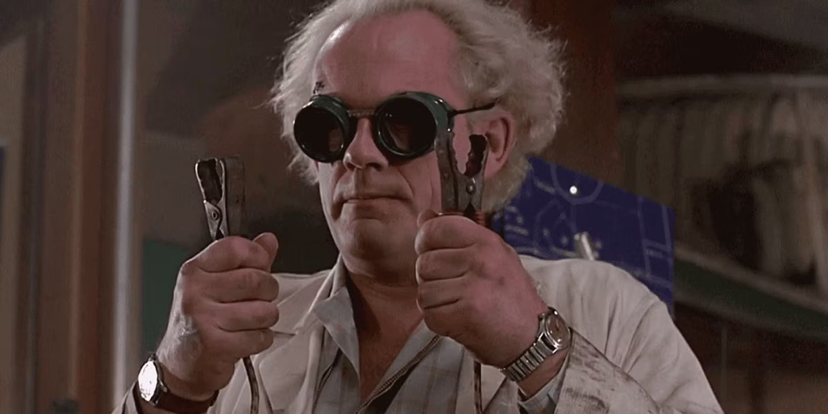Doc Brown de Retour vers le futur, lunettes de soudeur sur le nez, tenant deux pinces crocodiles et portant deux montres