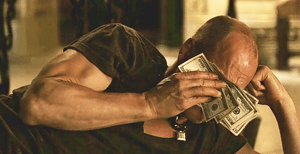 Homme chauve qui essuie ses fausses larmes avec une liasse de billets
