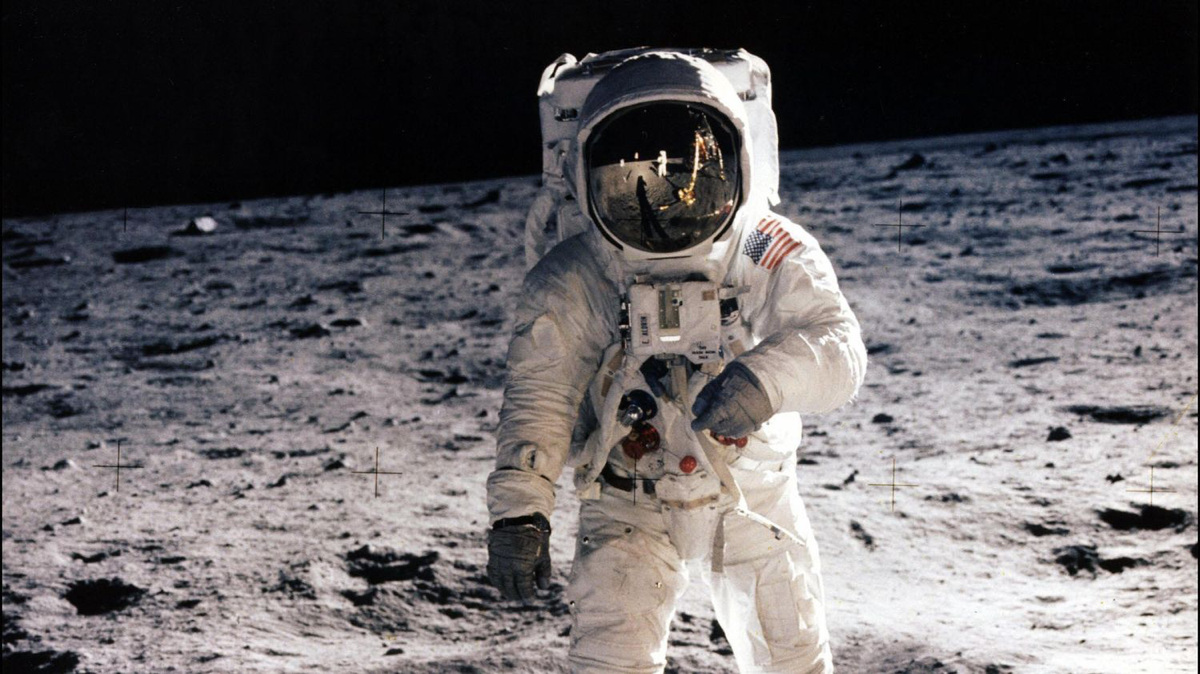 Astronaute d'Apollo 11 en combinaison blanche sur le sol lunaire, le module lunaire Eagle reflété dans la visière de son casque