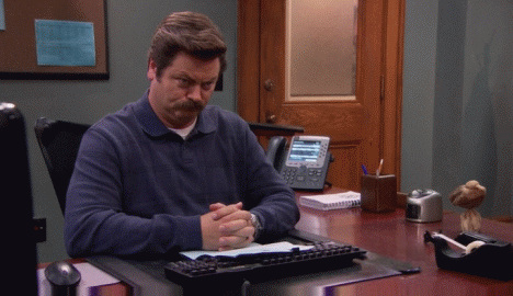 Ron Swanson assis à son bureau, mains jointes, attend en silence